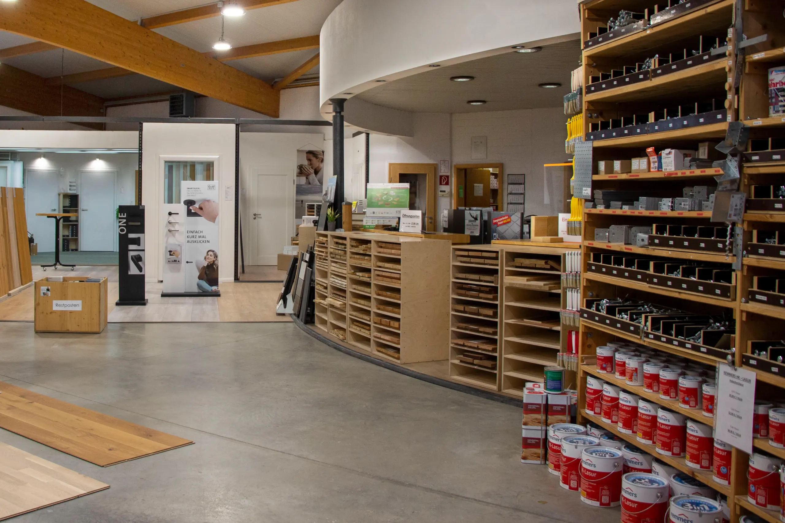 Eingangsbereich mit Theke und Ausstellung – Regale mit Schrauben und Farbtöpfen sichtbar.