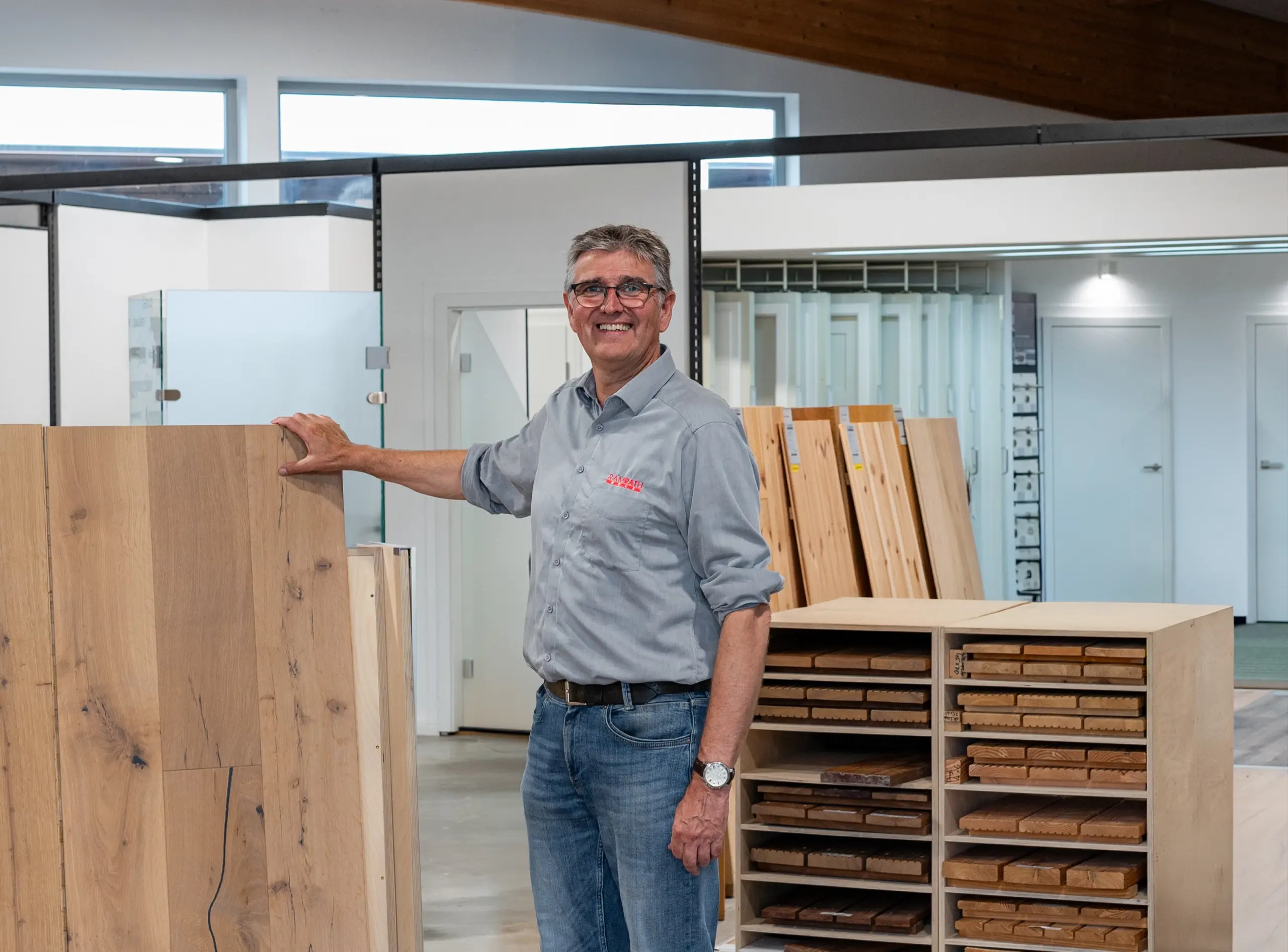 Frank Ramrath in der Bodenausstellung – zeigt lächelnd einen Parkettboden und heißt Besucher willkommen.
