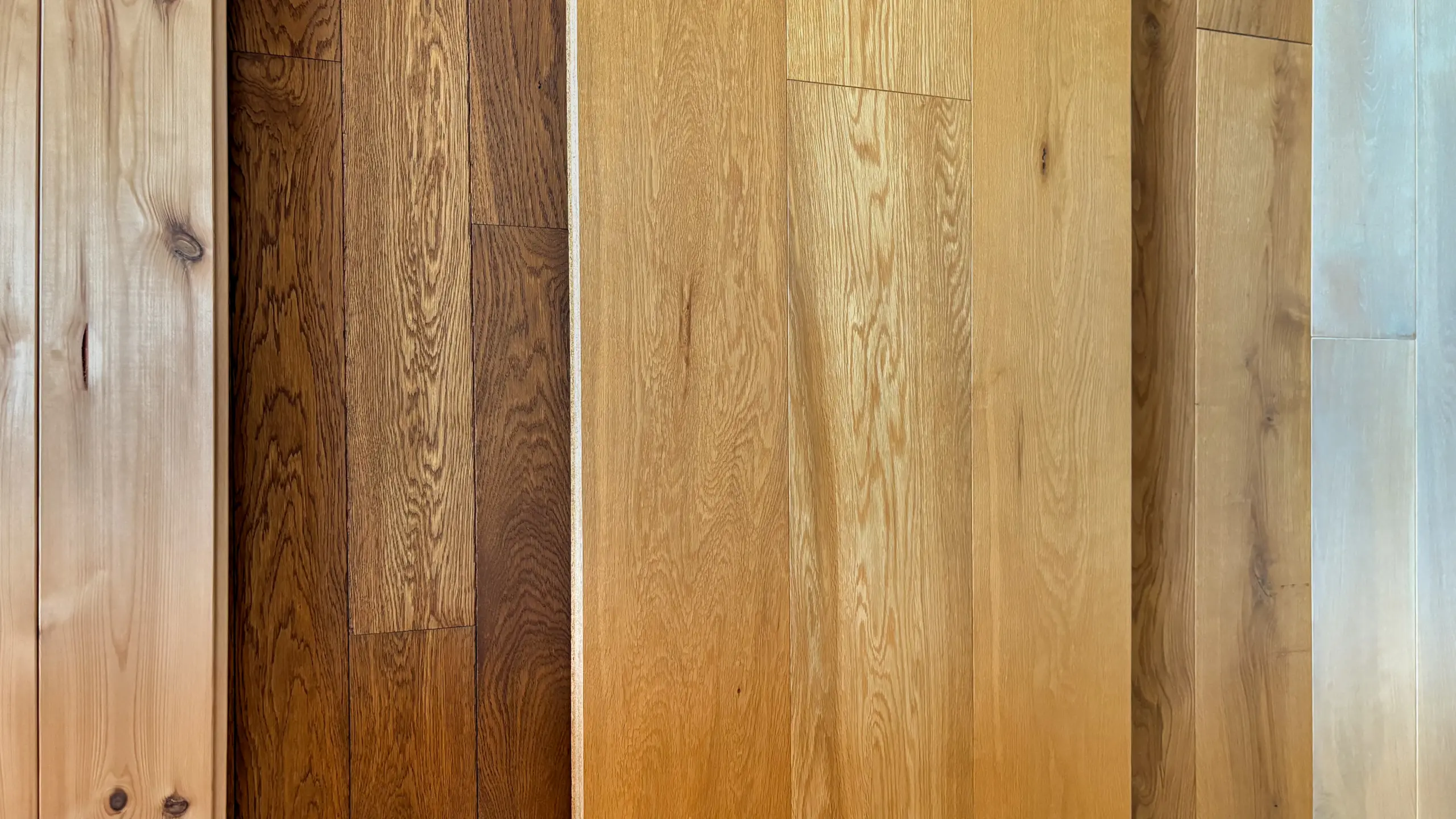 Massivholzdielen aus Eiche, Kiefer und Lärche in verschiedenen Farbtönen als Musterpräsentation nebeneinander ausgelegt.