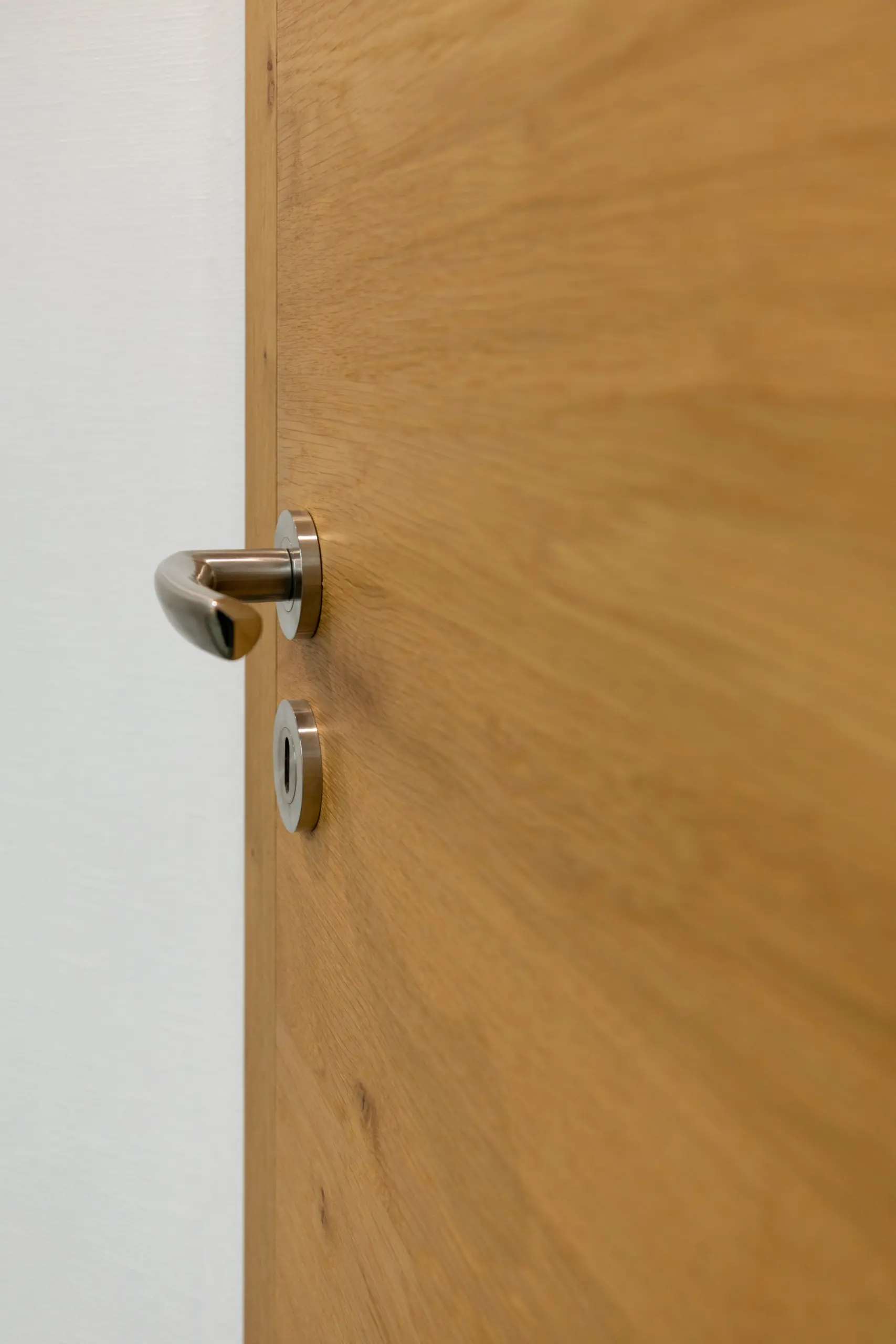 Stumpfeinschlagende Echtholztür ohne sichtbare Falz mit moderner Edelstahl-Drückergarnitur