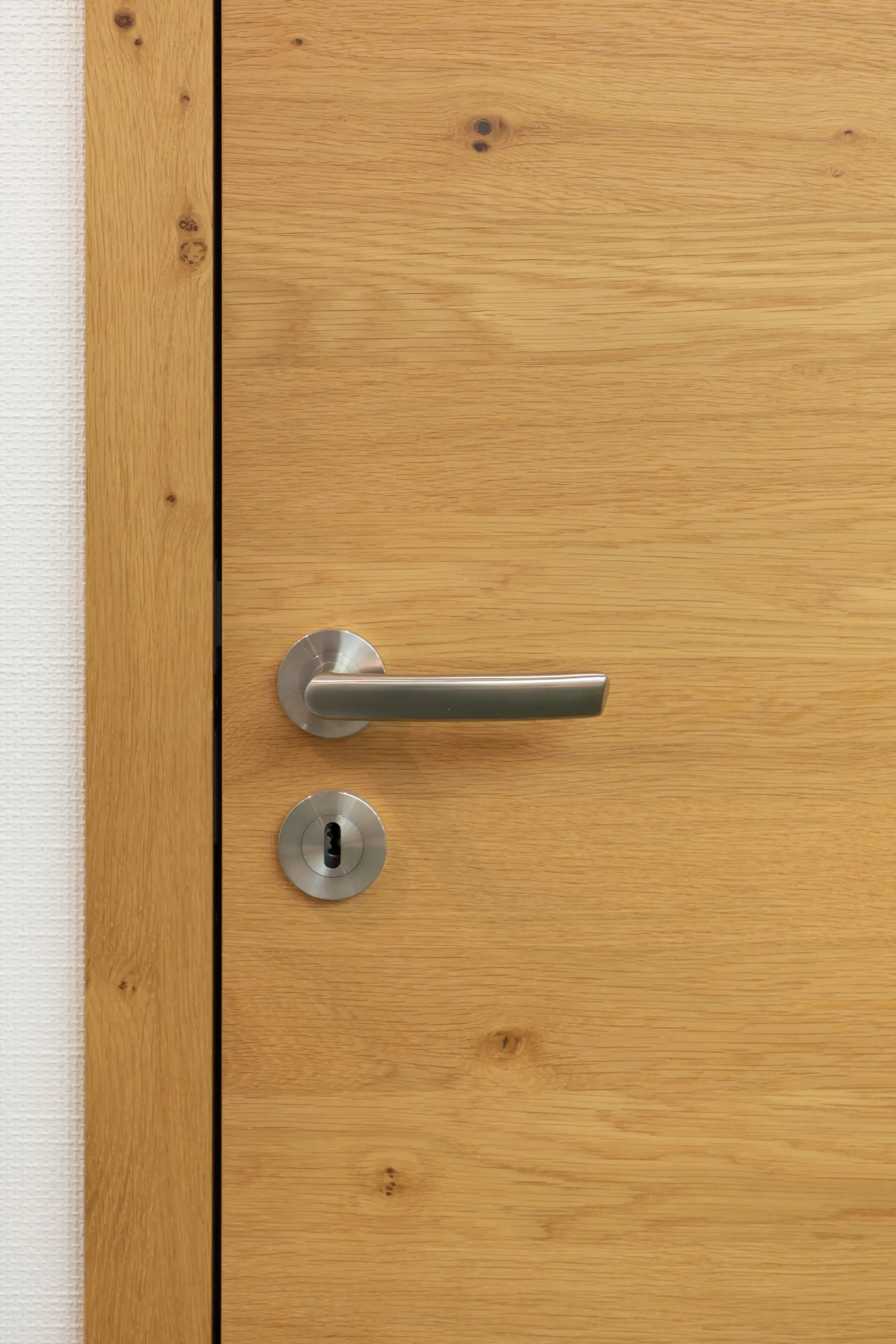 Stumpfeinschlagende Echtholztür ohne sichtbare Falz mit moderner Edelstahl-Drückergarnitur