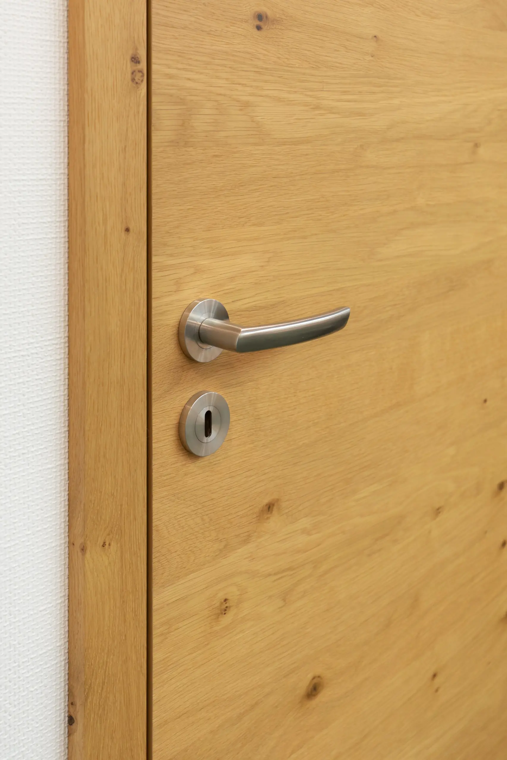 Stumpfeinschlagende Echtholztür ohne sichtbare Falz mit moderner Edelstahl-Drückergarnitur